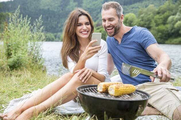 Happy couple with cell phone having a barbecue at lakeside model released Symbolfoto  FMKF002847