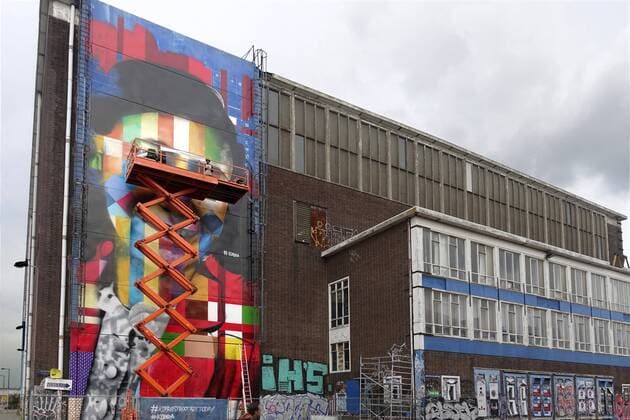 The Netherlands, Amsterdam. The famous Brazilian street artist Eduardo Kobra realizes this week a monumental portrait of Anne Frank, the man at the right side of the platform is Eduardo Kobra, 26 september 2016, Photo: Katrien Mulder Hollandse Hoogte Nederland, Amsterdam, Amsterdam Noord, NDSM Terrein, wereldberoende Braziliaanse streetartist Eduardo Kobra realiseert deze week een monumentaal portret van Anne Frank op de zuidelijke buitenmuur van de loods op de hoek van de MS van Riemsdijkweg, en de Tt Neveritaweg, , de man rechts in de hoogwerker is Eduardo Kobra  59396759