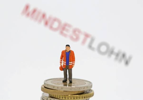 Nuernberg Symbolfoto, Themenbild Mindestlohn, Oeffentlicher Dienst, Arbeiter steht auf Euro Muenzen. Im Hintergrund der Schriftzug Mindestlohn in rot und schwarz. Copyright: xWuest Eibner-Pressefotox EP_FWT