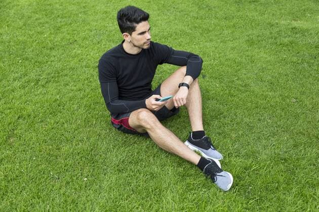 Jogger sitting in grass holding smartphone model released Symbolfoto  BOYF00639