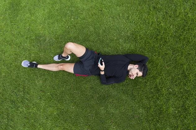 Jogger lying in grass holding smartphone model released Symbolfoto  BOYF00640