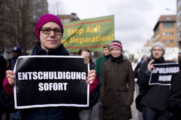 Gedenkmarsch Kolonialgeschichte DEU, Deutschland, Germany, Berlin, 25.02.2017 Demonstranten mit Plakat Apologise now, Entschuldigung sofort, beim 11. Gedenkmarsch zur Erinnerung an die afrikanischen Opfer von Versklavung, Kolonialismus und rassistischer Gewalt vom Komitee fuer ein afrikanisches Denkmal in Berlin und afrikanischer Vereine in Berlin. Dieser Gedenkmarsch wurde ins Leben gerufen, um der Forderung nach Anerkennung der Verbrechen gegen Schwarze Menschen und Menschen afrikanischer Herkunft Nachdruck zu verleihen. Anlass ist die Berliner Afrika-Konferenz von 1884 - 1885, auf der Afrika vor 130 Jahren unter den europaeischen Kolonialmaechten aufgeteilt wurde. Mehr als 30 Millionen Afrikanerinnen und Afrikaner wurden Opfer von Versklavung und kolonialen Verbrechen gegen die Menschlichkeit. Die von Deutschland an den Herero und Nama begangenen Voelkermorde in Namibia und die Kriegs