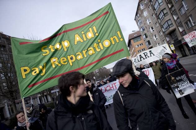 Gedenkmarsch Kolonialgeschichte DEU, Deutschland, Germany, Berlin, 25.02.2017 Demonstranten mit Transparent Stop Aid Pay Reparation beim 101 Gedenkmarsch zur Erinnerung an die afrikanischen Opfer von Versklavung, Kolonialismus und rassistischer Gewalt vom Komitee fuer ein afrikanisches Denkmal in Berlin und afrikanischer Vereine in Berlin. Dieser Gedenkmarsch wurde ins Leben gerufen, um der Forderung nach Anerkennung der Verbrechen gegen Schwarze Menschen und Menschen afrikanischer Herkunft Nachdruck zu verleihen. Anlass ist die Berliner Afrika-Konferenz von 1884 - 1885, auf der Afrika vor 130 Jahren unter den europaeischen Kolonialmaechten aufgeteilt wurde. Mehr als 30 Millionen Afrikanerinnen und Afrikaner wurden Opfer von Versklavung und kolonialen Verbrechen gegen die Menschlichkeit. Die von Deutschland an den Herero und Nama begangenen Voelkermorde in Namibia und die Kriegsverbreche