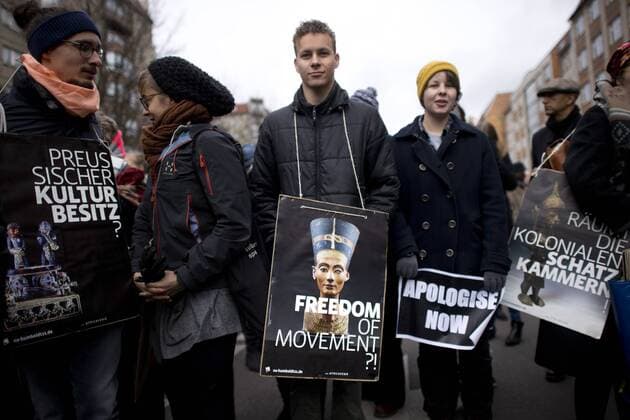 Gedenkmarsch Kolonialgeschichte DEU, Deutschland, Germany, Berlin, 25.02.2017 Demonstrant mit Plakat Freedom of Movement und Foto der Nofretete gegen die Kolobialgeschichte und die Aneigung afrikanischer Kulturgueter durch deutsche Museen und dem Humboldt Forum und Plakat Apologise now, Entschuldigung sofort, beim 11. Gedenkmarsch zur Erinnerung an die afrikanischen Opfer von Versklavung, Kolonialismus und rassistischer Gewalt vom Komitee fuer ein afrikanisches Denkmal in Berlin und afrikanischer Vereine in Berlin. Dieser Gedenkmarsch wurde ins Leben gerufen, um der Forderung nach Anerkennung der Verbrechen gegen Schwarze Menschen und Menschen afrikanischer Herkunft Nachdruck zu verleihen. Anlass ist die Berliner Afrika-Konferenz von 1884 - 1885, auf der Afrika vor 130 Jahren unter den europaeischen Kolonialmaechten aufgeteilt wurde. Mehr als 30 Millionen Afrikanerinnen und Afrikaner wur