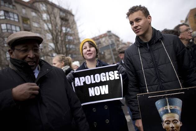 Gedenkmarsch Kolonialgeschichte DEU, Deutschland, Germany, Berlin, 25.02.2017 Demonstrant mit Plakat Freedom of Movement und Foto der Nofretete gegen die Kolobialgeschichte und die Aneigung afrikanischer Kulturgueter durch deutsche Museen und dem Humboldt Forum und Plakat Apologise now, Entschuldigung sofort, beim 11. Gedenkmarsch zur Erinnerung an die afrikanischen Opfer von Versklavung, Kolonialismus und rassistischer Gewalt vom Komitee fuer ein afrikanisches Denkmal in Berlin und afrikanischer Vereine in Berlin. Dieser Gedenkmarsch wurde ins Leben gerufen, um der Forderung nach Anerkennung der Verbrechen gegen Schwarze Menschen und Menschen afrikanischer Herkunft Nachdruck zu verleihen. Anlass ist die Berliner Afrika-Konferenz von 1884 - 1885, auf der Afrika vor 130 Jahren unter den europaeischen Kolonialmaechten aufgeteilt wurde. Mehr als 30 Millionen Afrikanerinnen und Afrikaner wur