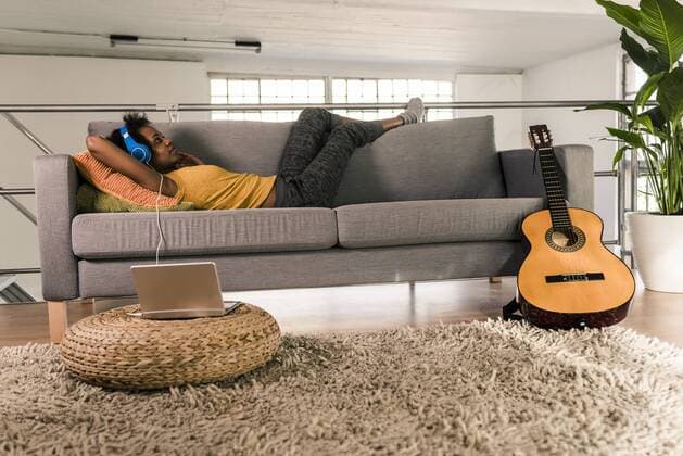 Young woman lying on couch with headphones connected to laptop model released Symbolfoto property released  UUF10328