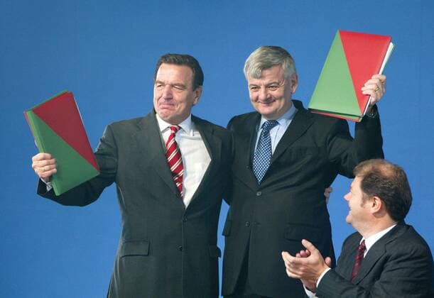 Unterschrift unter die Koalitionsvereinbarung zwischen SPD und Gruene : Bundeskanzler Gerhard Schroeder (l), SPD, und Bundesaussenminister Joschka Fischer, Gruene, umarmen sich. Es applaudiert Olaf Scholz, designierter SPD Generalsekretaer. Berlin, 16.10.2002, Berlin Deutschland Copyright: xThomasxKoehlerx