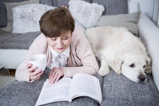 Senior woman lying on couch, reading book with dog by her side model released Symbolfoto property released  WESTF23278