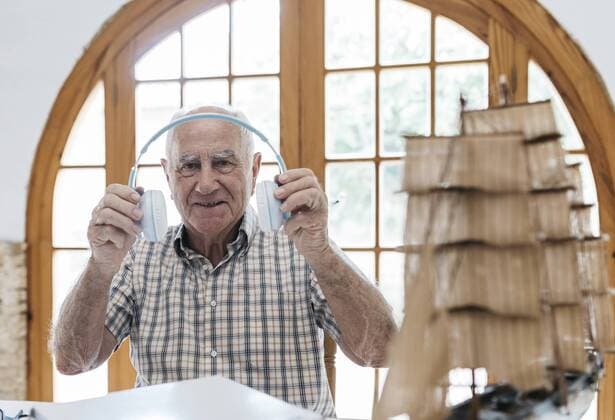 Portrait of confident senior man unpacking headphones from package with model ship on table model released Symbolfoto property released  JRFF01411