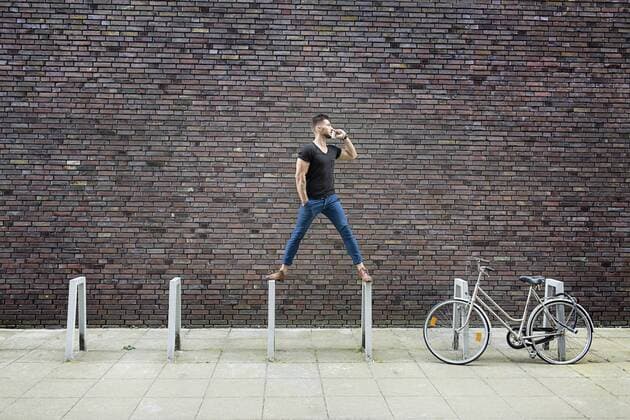 Man with cell phone balancing on bicycle rack in front of brick wall model released Symbolfoto  DMOF00019