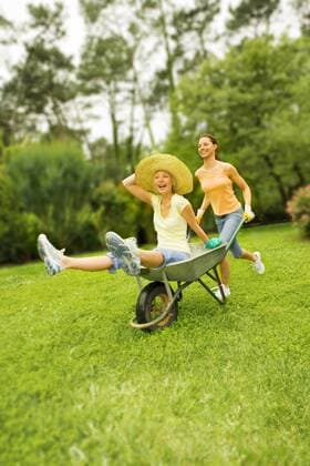 Two young women in the garden having fun with a wheel barrow  A5