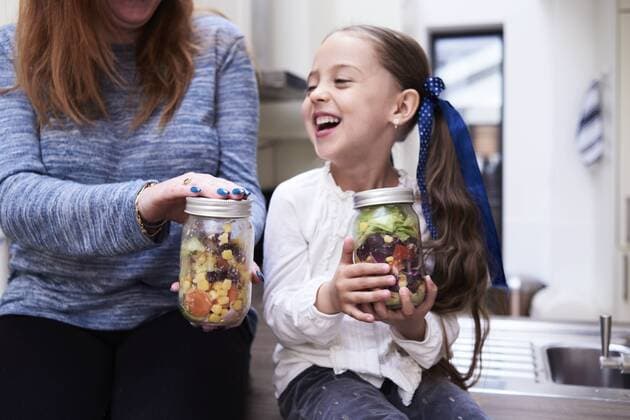 Laughing little girl with preserving jar of mixed salad sitting beside her mother model released Symbolfoto property released  IGGF00005
