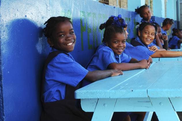St Lucia, Canaries, schoolgirls in a row sitting on a bench against a blue wall  Copyright: xDanitaDelimont.com