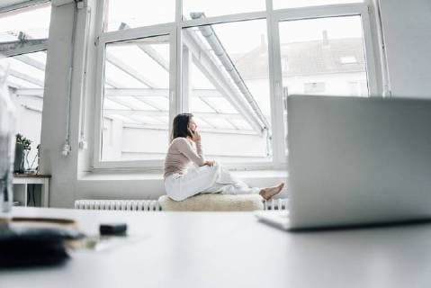 Young woman on the phone sitting on sheepskin on heater in a loft looking out of window model released Symbolfoto property released  MOEF00446