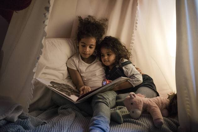 Two sisters sitting in dark children s room, reading a book model released Symbolfoto property released  MOEF00404