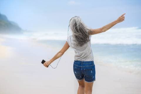 Senior woman with headphones dancing on the beach model released Symbolfoto  SBOF01098