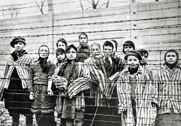 Surviving Jewish children in Auschwitz with nurse behind barbed wire fence. The photo was taken by a soviet photographer while making a film about liberation of the camp. The children were disguised by the Russians with clothes of adult prisoners. Auschwitz Poland. Date of February, 1945