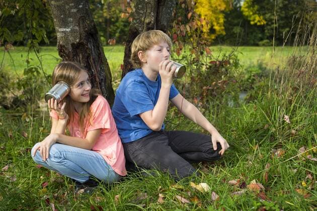 Boy and girl on a meadow having fun with tin can phone model released Symbolfoto  SARF03559