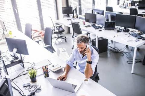 Mature businessman sitting at desk in office using cell phone and laptop model released Symbolfoto property released  HAPF02680
