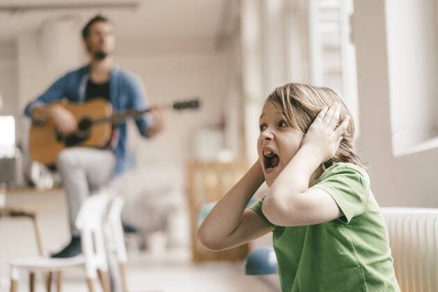 Horrified son covering his ears with father playing guitar at home model released Symbolfoto property released  KNSF03636