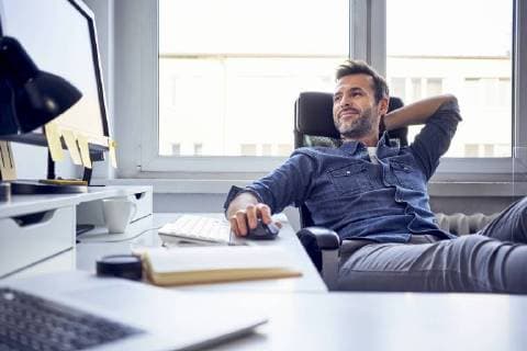 Relaxed man sitting at desk in office looking at computer screen model released Symbolfoto property released  BSZF00256