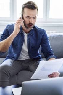 Serious man with documents and laptop on sofa talking on cell phone model released Symbolfoto property released  BSZF00283
