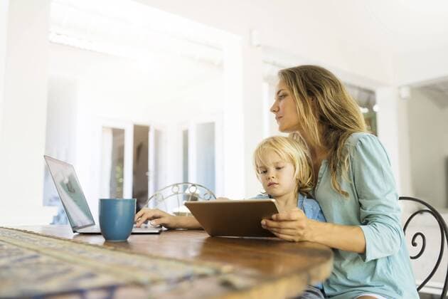 Boy sitting on his mother s lap and looking at a tablet while his mother is working on a laptop model released Symbolfoto property released  SBOF01459