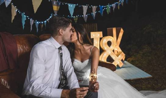 Romantic wedding couple sitting on sofa kissing while holding sparklers in their hands on a night party outdoors model released Symbolfoto property released  DAPF00956