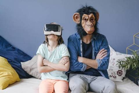 Father wearing monkey mask sitting next to son wearing VR glasses at home model released Symbolfoto property released  KNSF03647