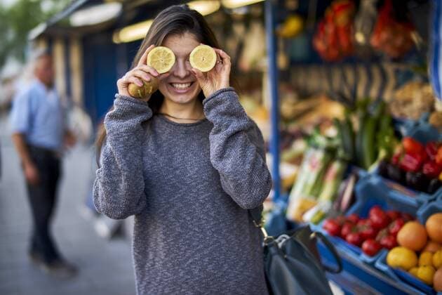 Laughing young woman on market covering her eyes with lemon halves model released Symbolfoto  BEF00084