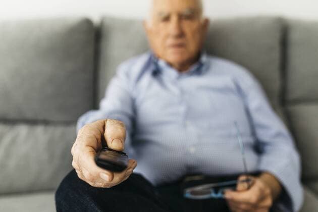 Senior man watching TV from the couch at home, focused on hand model released Symbolfoto property released  JRFF01672