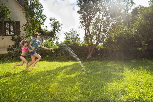 Girl and her little sister having fun with lawn sprinkler in the garden model released Symbolfoto property released  LVF07056