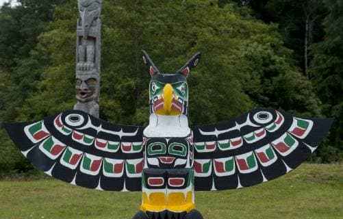 Thunderbird and Man holding copper by Bruce Alfred, older poles behind, at Namgis Burial grounds, Alert Bay, Cormorant Island, Vancouver Island, British Columbia, Canada  acp105297 ChrisxCheadle