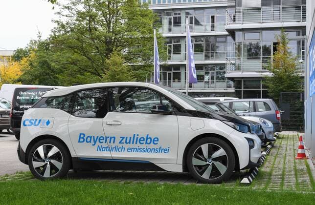 An electric vehicle with the lettering Bayern sake CSU stands at a charging station E charging station n and lettering on Franz Josef Strauss House of the CSU headquarters in Munich
