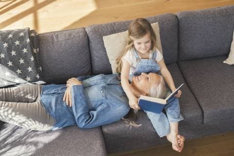 Grandmother and granddaughter sitting on couch, reading together a book model released Symbolfoto property released  SBOF00538
