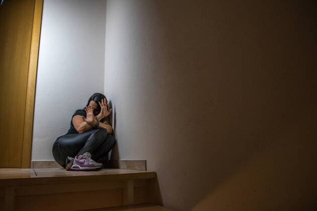 Young dark-haired woman huddled warding off domestic violence with hands symbol image Domestic violence against women symbol photo