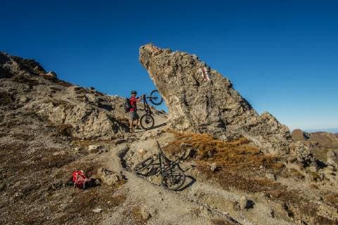 A mountain biker stands with his bike on a striking rock on the climb just before the pass of the Wissmilen Pass 2420 m in the area Flumserberg Canton St Gallen Switzerland MTB Tour in the Swiss Alps