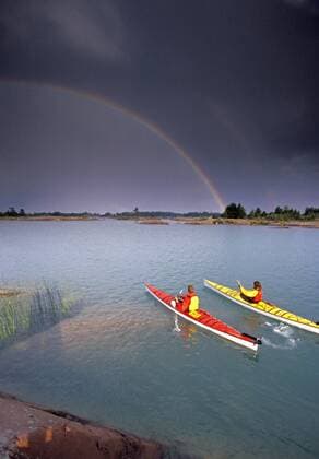 Young couple sea-kayaking through archepelago of granite islands of Canadian Shield in Georgian Bay, Lake Huron near Philippe Edward Island, Ontario, Canada. A passing thunder storm results in a double rainbow. (Photo by Henry Georgi Aurora), Killarney Ontario Canada model released Symbolfoto Copyright: HenryxGeorgi 8790500024