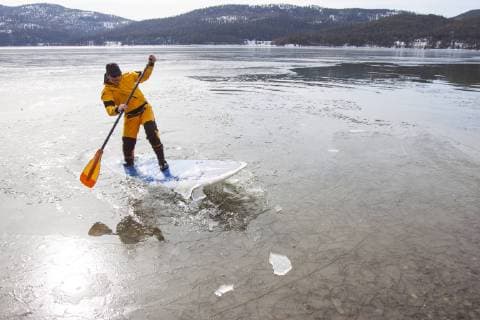 IMAGO Creative, Winter, Winterspaß, Eishockey A fit male in a dry suit paddles his stand up paddle board (SUP) through a thin sheet of ice covering Whitefish Lake in Whitefish, Montana., Whitefish Montana USA model released Symbolfoto Copyright: CraigxMoore MOCR000200