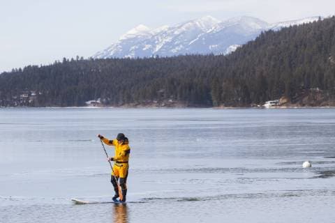 IMAGO Creative, Winter, Winterspaß, Eishockey A fit male in a dry suit paddles his stand up paddle board (SUP) through a thin sheet of ice covering Whitefish Lake in Whitefish, Montana., Whitefish Montana USA model released Symbolfoto Copyright: CraigxMoore MOCR000204