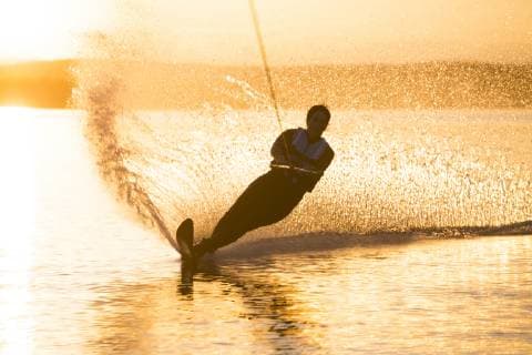 IMAGO Creative: Sport Dichotomien - Land und Wasser A woman cuts a turn while water skiing at sunset on Whitefish Lake in Whitefish, Montana., Whitefish Montana USA model released Symbolfoto Copyright: CraigxMoore MOCR000382