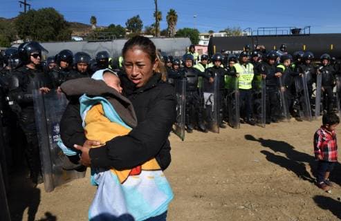 November 25, 2018 - Tijuana, Mexico - ROSA VILLA and her baby ESTEBAN, 5 months old, walk past Mexican police in riot gear moving the migrants away from the border. They are from Honduras. They were met by a line of Mexican police in riot gear at the bridge but managed to run past them, climbing up steep walls, crossing the Rio Tijuana and difficult terrain, reaching the border but were met at times by tear gas from U.S. agents when they tried to climb over fence and were pleading to be let in. Eventually Mexican police moved the crowd, including many women and children back to the shelter. Tijuana Mexico - ZUMAg208 20181125_zap_g208_056 Copyright: xCarolxGuzyx