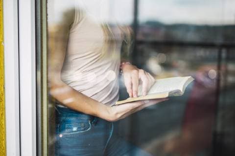 Close-up of young woman reading a book behind windowpane model released Symbolfoto property released  KKAF01992