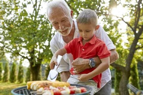 Grandfather helping grandson turning a corn cob during a barbecue in garden model released Symbolfoto property released  ZEDF01601