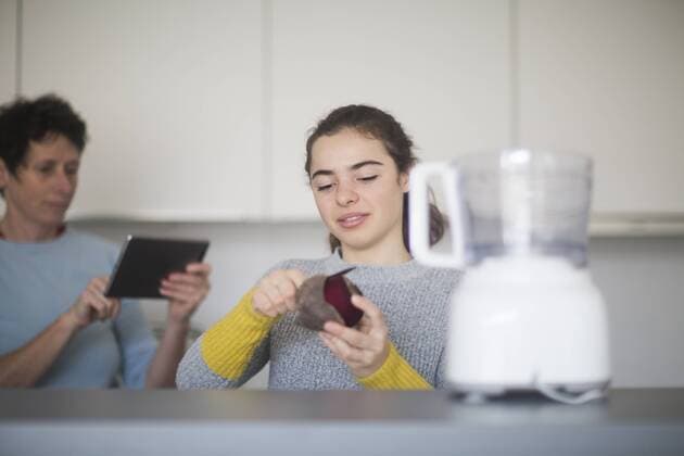 Portrait of smiling young woman peeling beetroot in the kitchen while mother using tablet in the background model released Symbolfoto property released  SGF02133