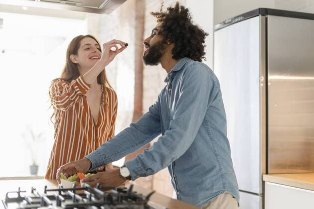 Couple standing in kitchen, preparing dinner party, woman feeding man with olive model released Symbolfoto property released  ERRF00530
