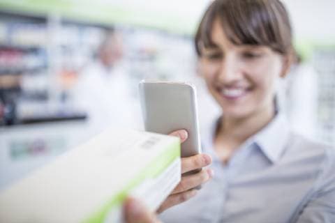 Smiling woman in pharmacy holding smartphone and medicine model released Symbolfoto property released  WESTF23982