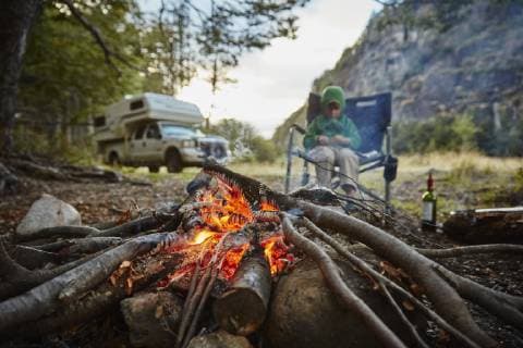 IMAGO Creative: Herbst, Touren mit dem Camper Chile, Santa Magda, Rio Maniguales, boy sitting at campfire in forest with camper van in background model released Symbolfoto property released  SSCF00224