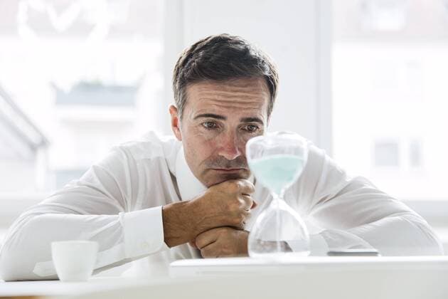 Serious businessman looking at hourglass on table in office model released Symbolfoto property released  MOEF01452
