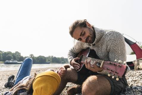 Happy young couple playing guitar at a tent at the riverside model released Symbolfoto  UUF15404